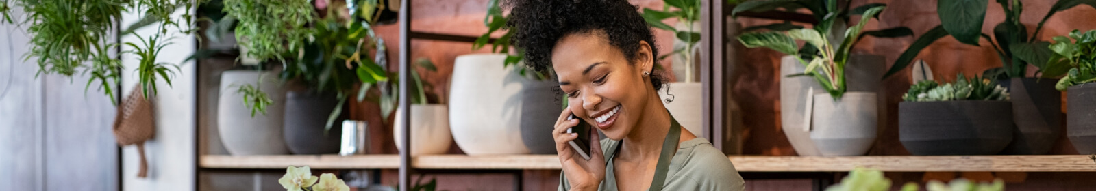 Woman in plant shop smiling behind the counter while on the phone