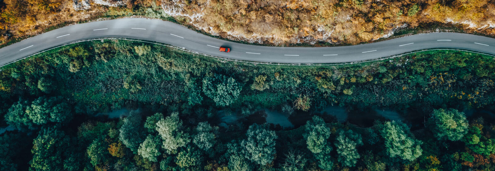 Winding road nestled between mountain and forest with a single car driving on it