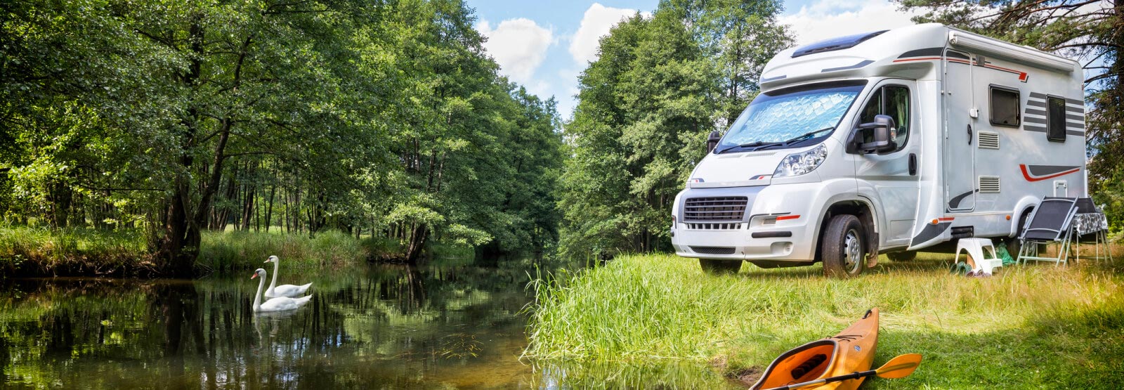 RV parked in a remote area with camp set up next to a pond with swans swimming