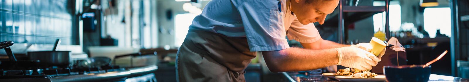 Chef adding sauce to a dish in a restraunt kitchen