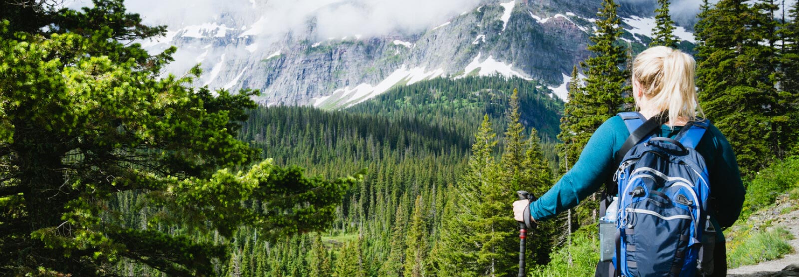 Woman hiking in green forest with foggy mountain scape ahead