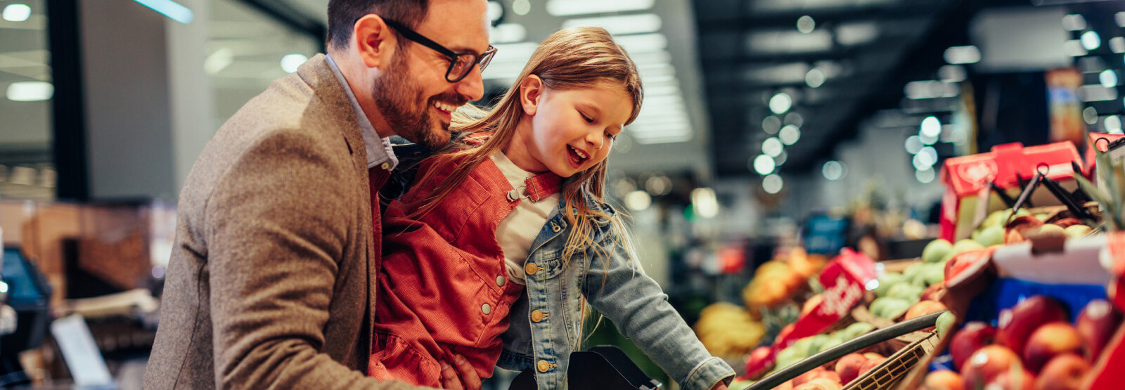 Father and daughter smiling at grocery store while picking up produce