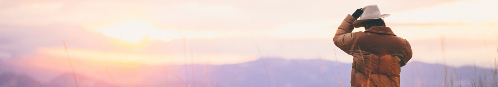 Man in cowboy hat facing a sunset 