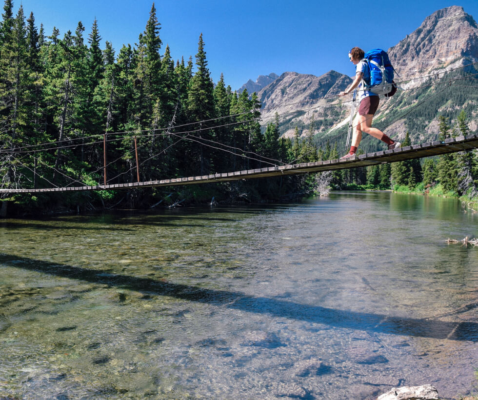 Person on a hike walking on a rope bridge that crosses over a stream