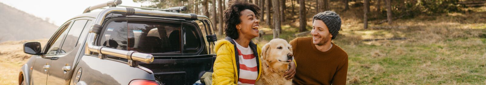 Couple and their dog sitting in the bed of their truck smiling together while traveling through a remote forest location